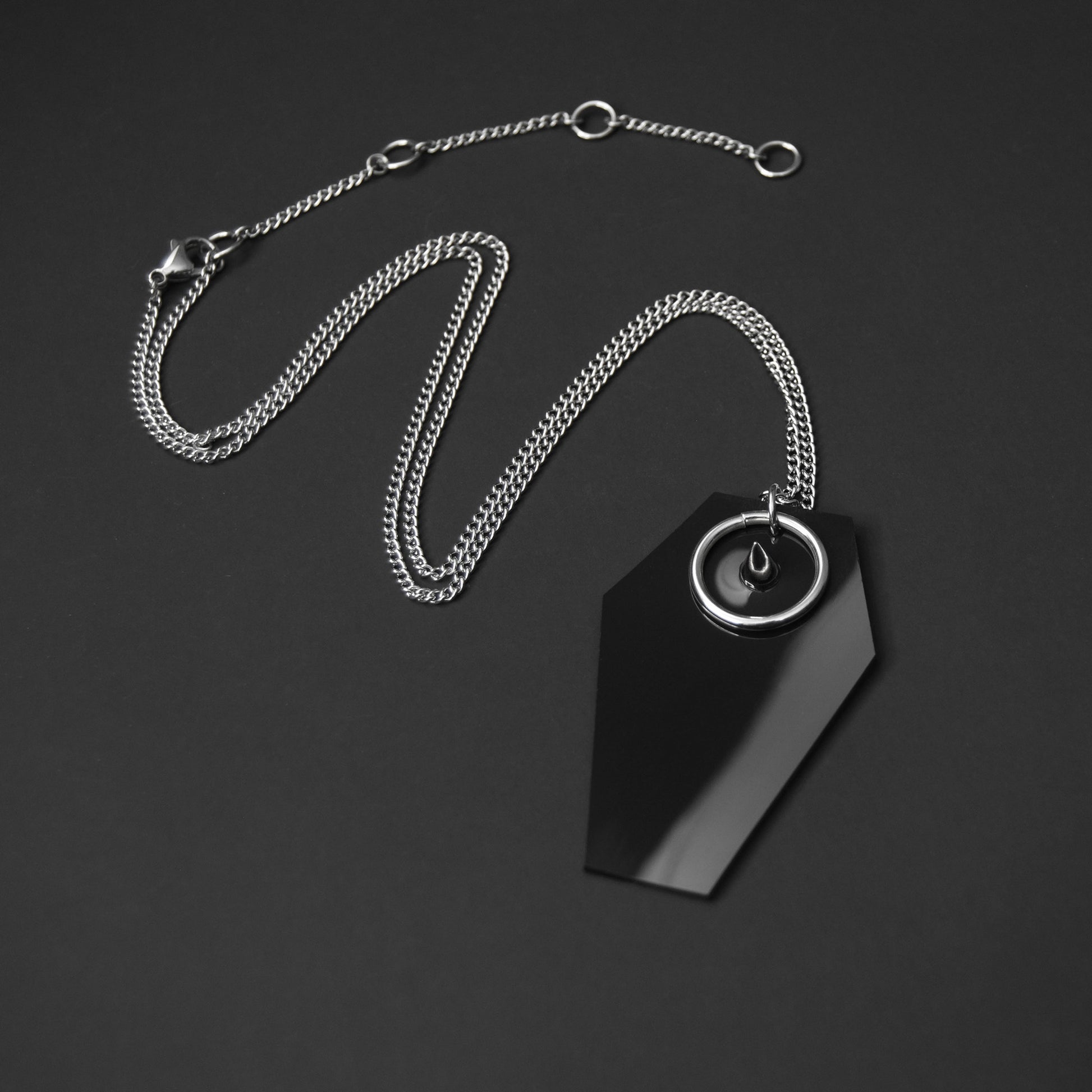 Gothic-style necklace featuring a black PVC coffin-shaped pendant with a silver spike and O-ring, suspended from an adjustable stainless steel chain.