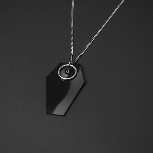 Close-up of a black PVC coffin-shaped pendant with a silver spike and O-ring, showcasing gothic-inspired details.