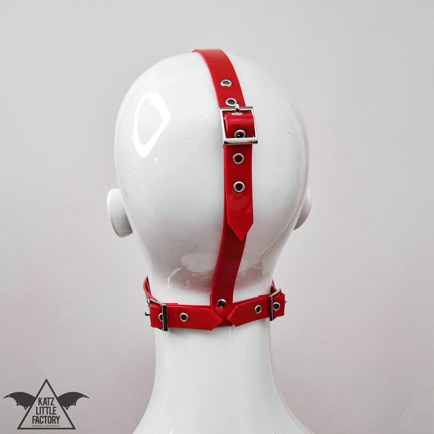 Back view of a gothic red PVC muzzle head harness, highlighting the adjustable straps and buckle fastening.