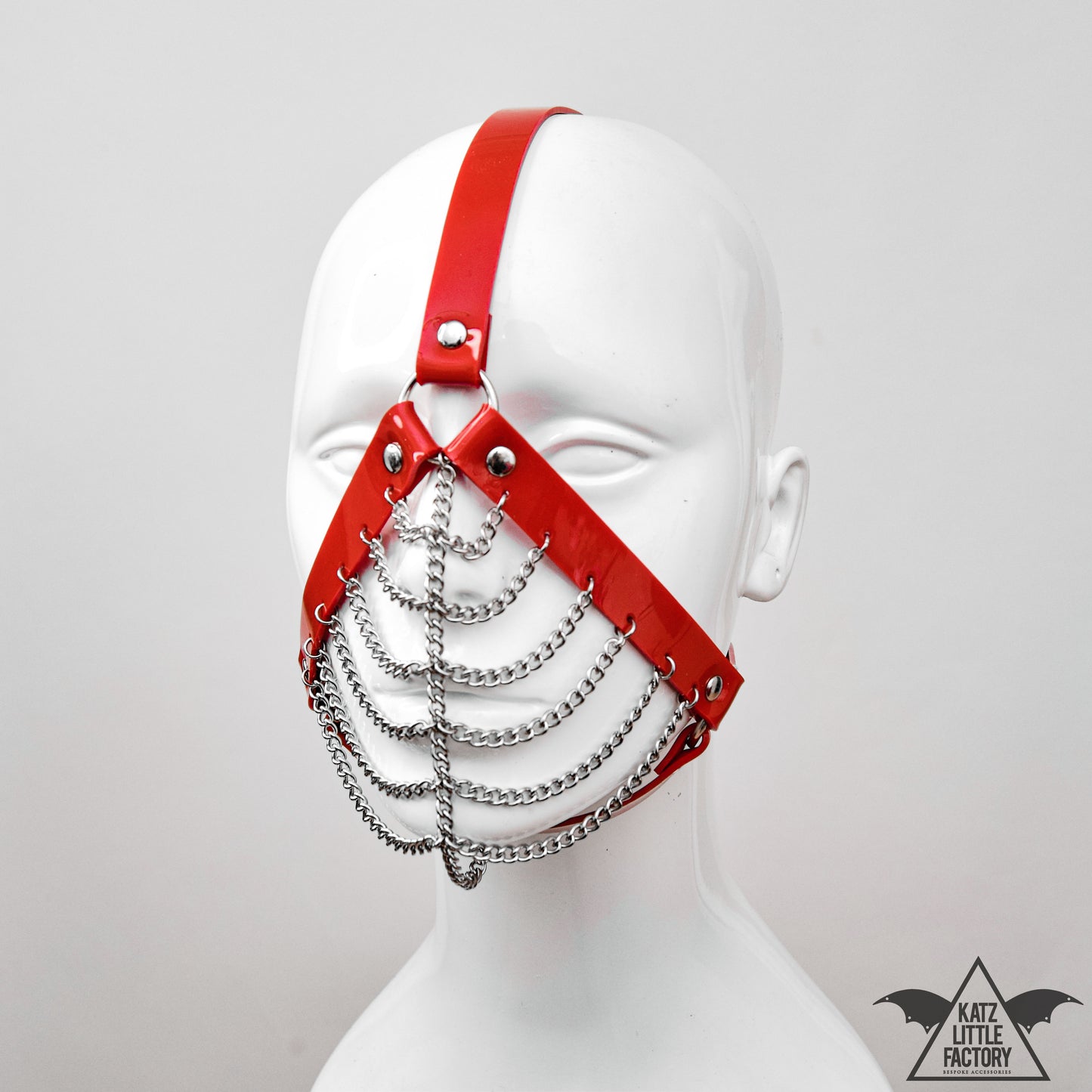 Profile of a gothic red PVC muzzle head harness with stainless steel chains over the mouth and nose.