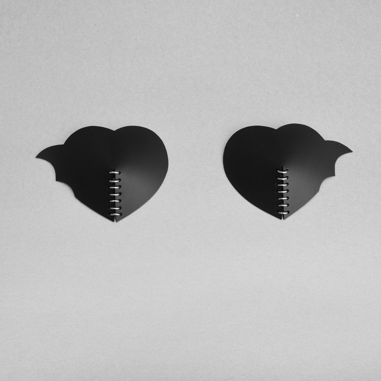 A pair of gothic black heart PVC breast petals with asymmetric bat wing design and a central row of jump rings.