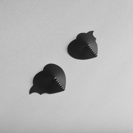 A pair of gothic black heart PVC breast petals with asymmetric bat wing design and a central row of jump rings, at a jaunty angle.