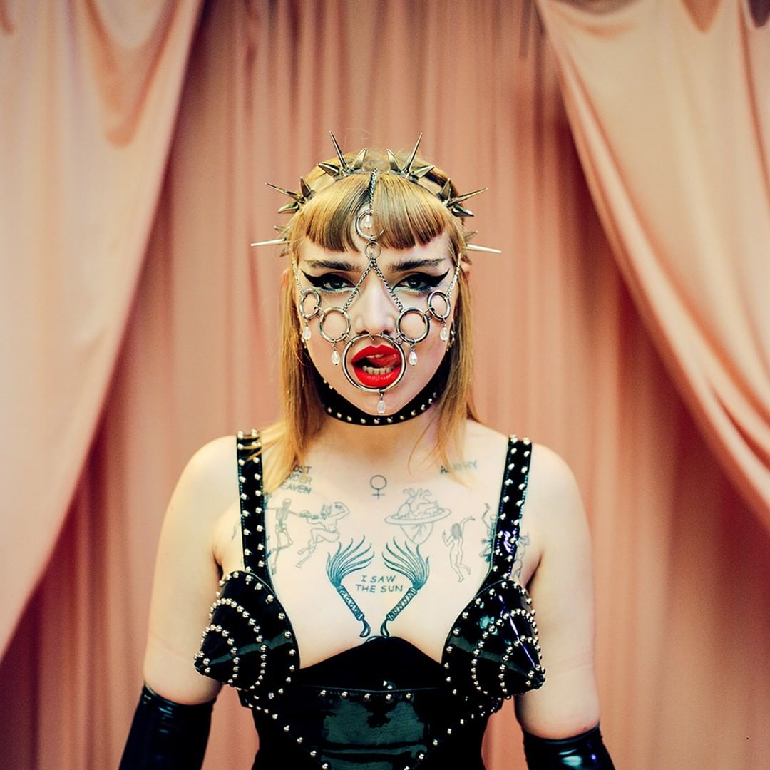 Gothic fetish model wearing a spike crown headdress with a rings mouthpiece decorated with crystals.