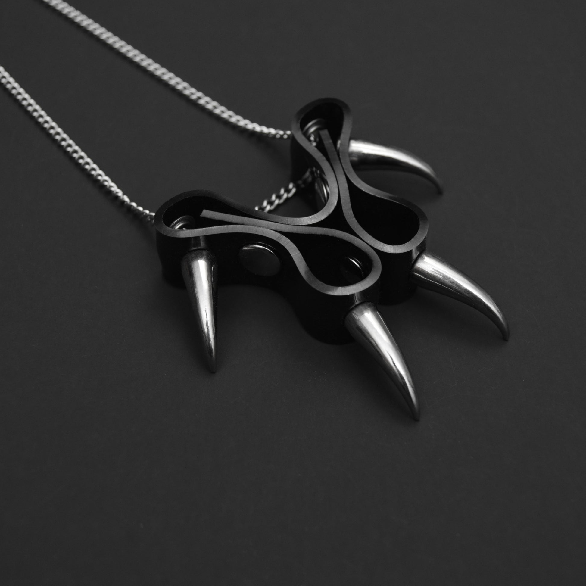Close-up of a black PVC cat claw-style pendant with silver claw spikes, featuring a matching silver chain necklace in an elegant gothic style.