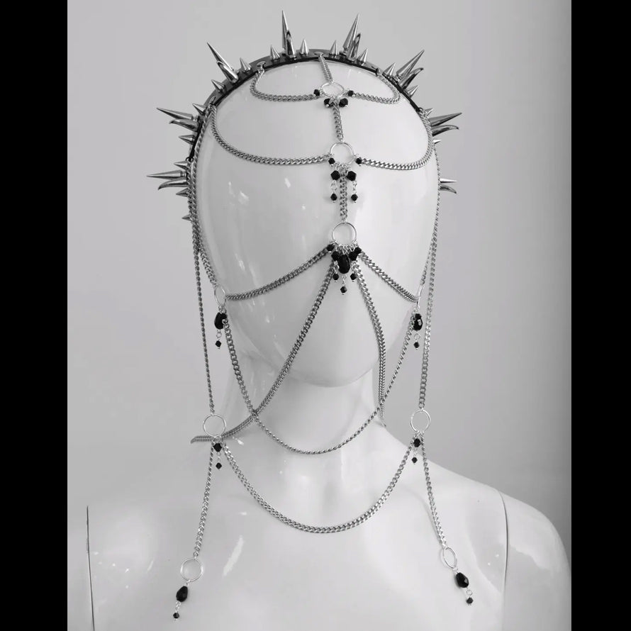 Close-up of a metal chains and black bead headpiece with sharp metal spikes, displayed on a white mannequin. The headpiece is showcased in a studio setting with a plain background, emphasizing its gothic and alternative design.