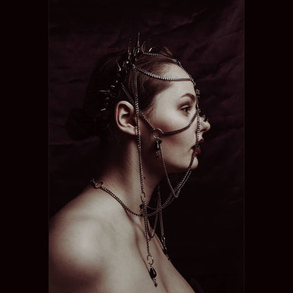 Young woman wearing an elaborate metal headpiece, made up of chains, black glass beads, and a spiked headpiece.