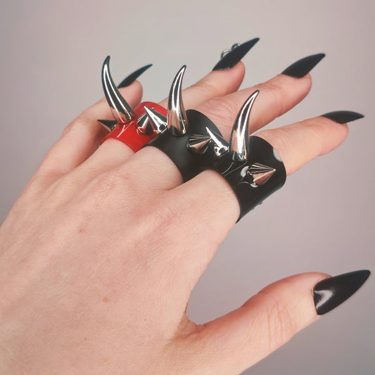 Three gothic PVC spike rings in gloss black, matte black, and red, with a central claw-like spike.