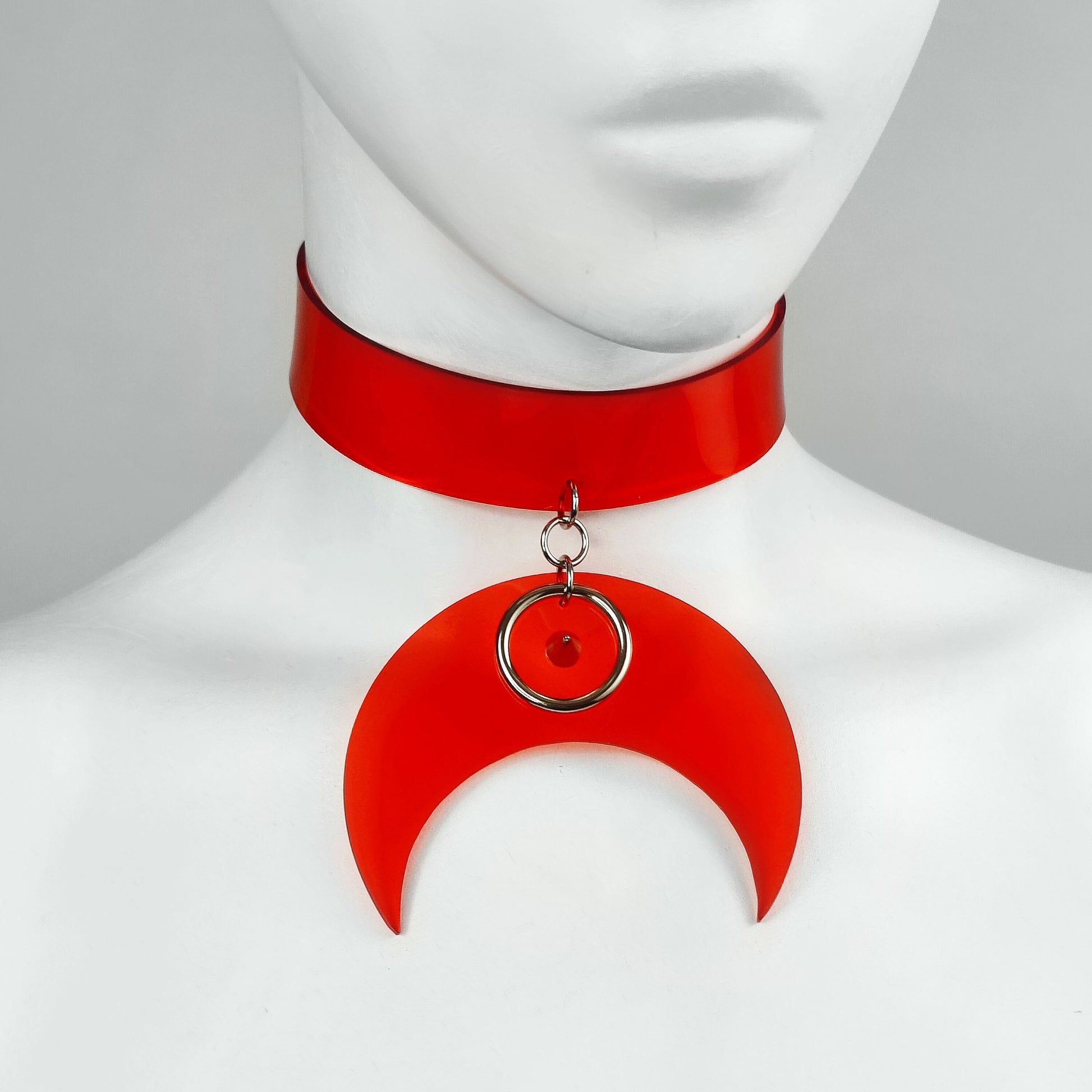 Translucent red vinyl choker with crescent pendant decorated with metal o ring and a spike centre studded detail.