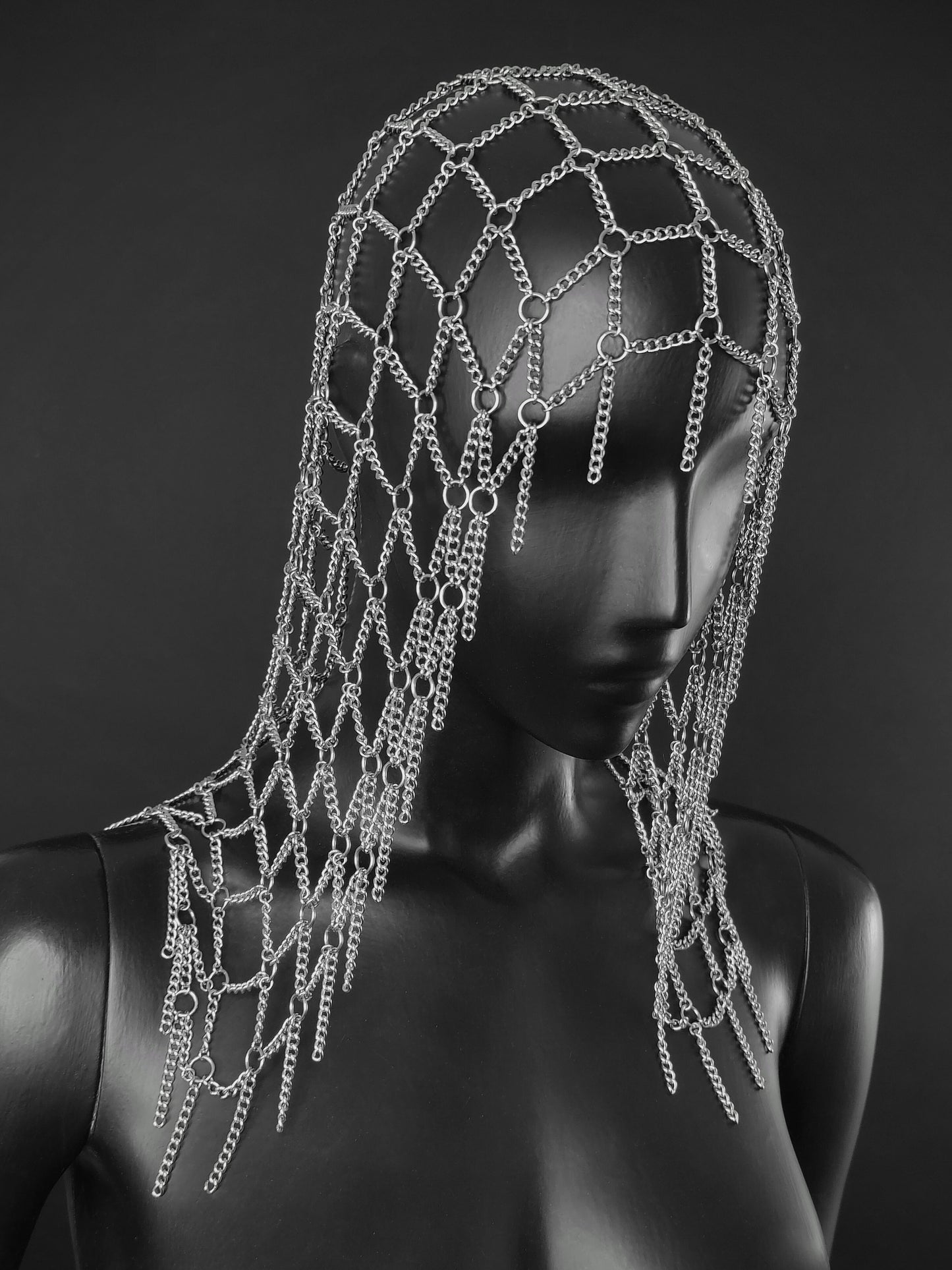 A silver chain fantasy inspired headpiece displayed on a black mannequin head and shoulders against a dark gray studio background.