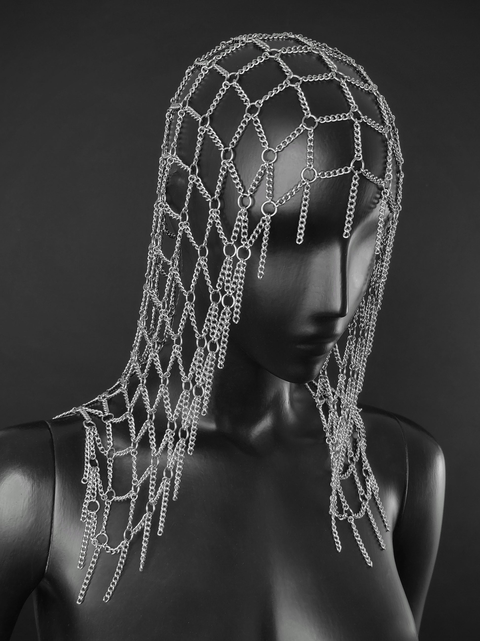 A silver chain fantasy inspired headpiece displayed on a black mannequin head and shoulders against a dark gray studio background.