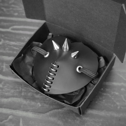 Black heart shape costume eye patch with spike, rings and studs decoration.