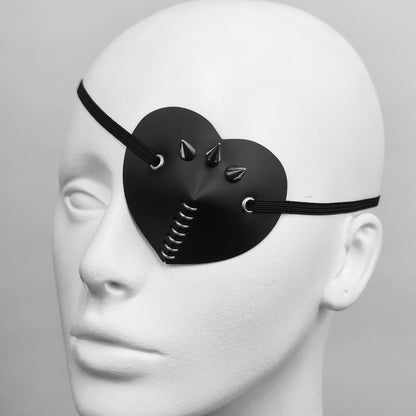 Black heart shape eye patch with spike, rings and stud details.
