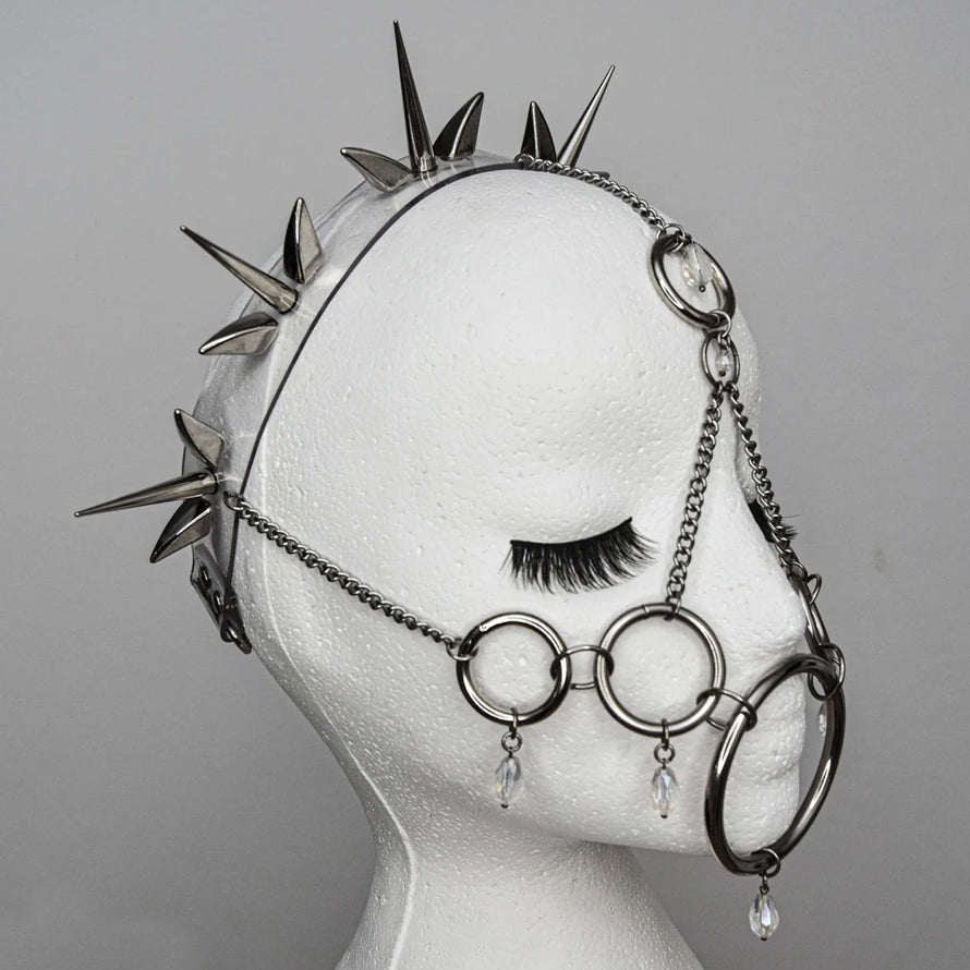 Mannequin head wearing a complex metal headpiece featuring a spiked crown and interconnected rings forming a muzzle-like mask. The intricate, dark, and edgy design is highlighted against a plain background, emphasizing its alternative and fetish-inspired aesthetic.