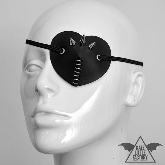 A white mannequin head with a black heart-shaped eye patch, featuring a cluster of spikes