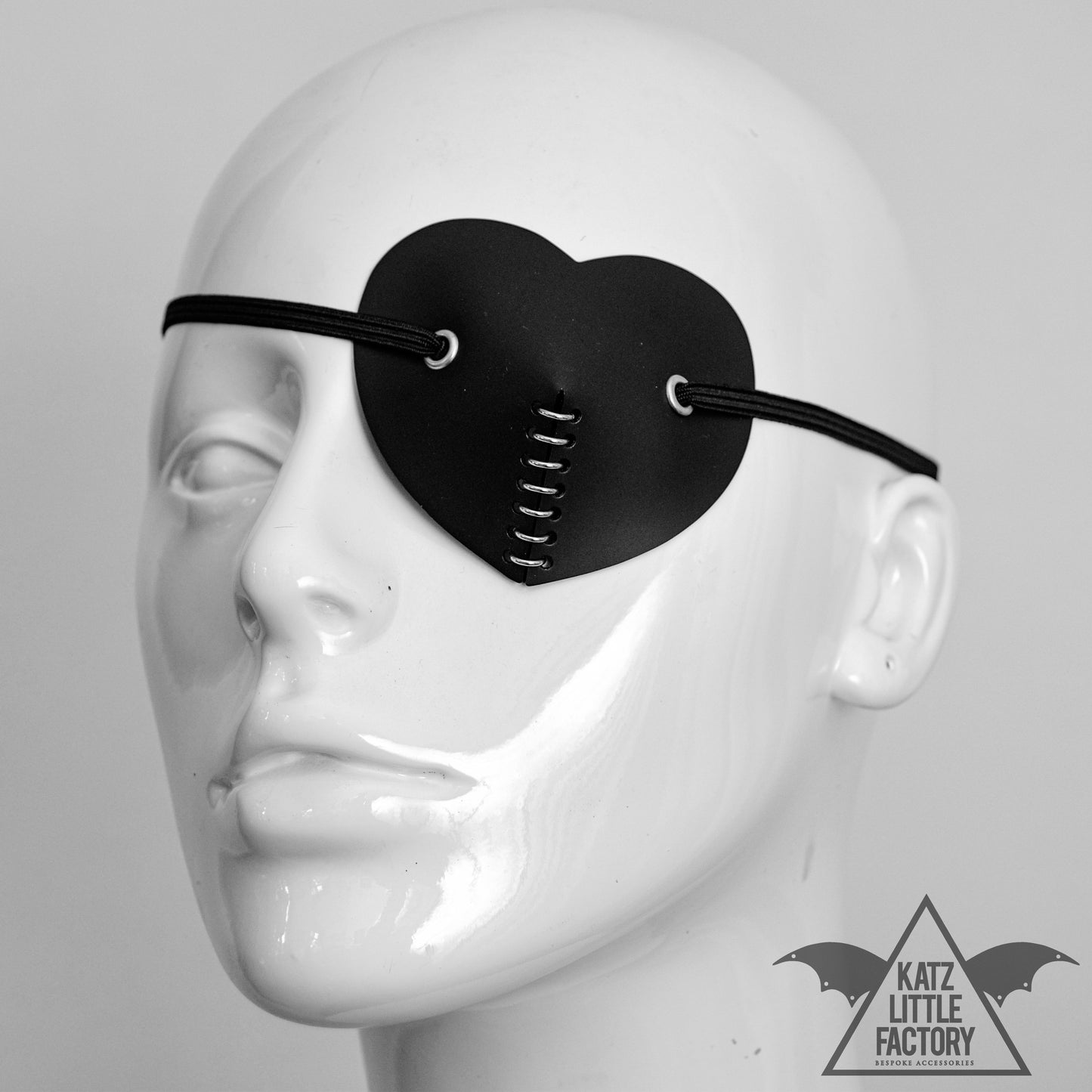 A black heart shaped eye patch on a mannequin, with a line of rings