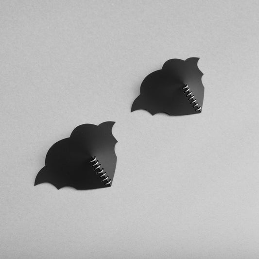 A pair of gothic black heart PVC breast petals with symmetrical bat wings and a central row of jump rings. at an angle.