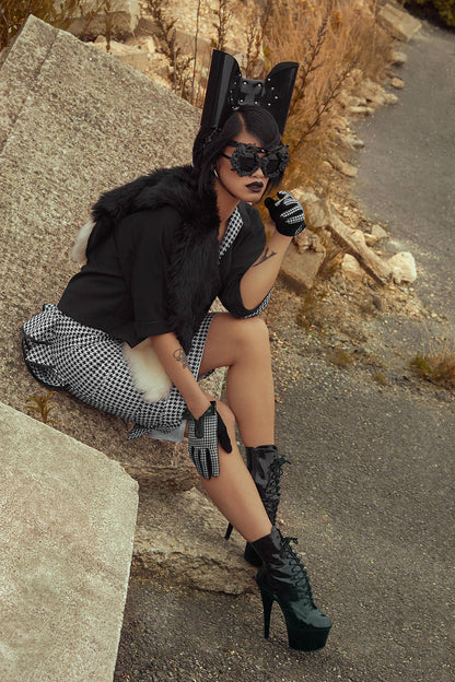 Oversized studded PVC bow headband on a person with black faux-fur and a gingham skirt.
